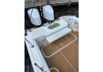 Twin outboard motors raised above the white boat stern, with a fold-down seating bench and teak deck, near a dock.