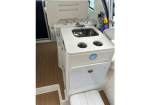 Compact boat galley with a small sink, two-burner stove with cover, and built-in cup holders on a teak deck.