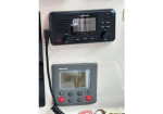 Garmin marine radio mounted on a boat wall above a Raymarine control unit with display and red/black buttons.