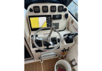 Boat helm with chrome steering wheel, navigation screen, and control gauges on a beige dashboard.