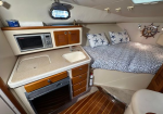 Compact boat galley and cabin bed: microwave, sink, stove, drawers, and a bed with starfish-pattern pillows.