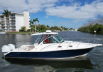 A white and navy motorboat cruising on a calm canal with palms and a white apartment building in the background.