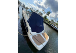White motorboat with a blue canopy tied to a dock, calm water, palm trees and buildings in the background.