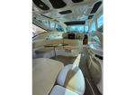 Luxurious boat cabin interior with cream leather seating around a table, curved counters, and large windows letting in daylight.