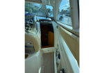 Interior of a small boat cockpit with the helm and dashboard on the left and an open hatch leading to the cabin below deck