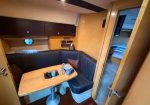 Cozy boat cabin with an L-shaped blue upholstered seating area around a wooden rectangular table.