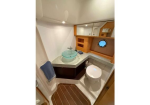 Compact boat bathroom with a teal glass vessel sink, wooden cabinetry, and a porthole window beside the toilet.