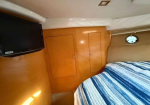 Cozy cabin interior featuring a wall-mounted TV, two wooden cabinet doors, a bed with a blue striped quilt, and a small round porthole window.