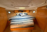 Boat cabin bedroom with a striped blue-and-white bed, built-in wooden cabinetry, and porthole windows.