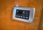 Wall-mounted climate control panel on a wooden wall, with display and buttons showing auto settings.