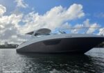 A sleek white motor yacht floating on calm water under a partly cloudy sky, viewed from a low side angle with a forward deck and railing visible.