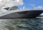 Low-angle view of a white and dark gray motor yacht on calm water, with an open cockpit canopy and stainless railing along the bow.