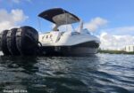 White motor yacht with two large black fenders at the stern, on calm water under a blue sky with clouds.