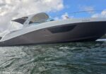Low-angle view of a white and dark gray motor yacht on calm water under a blue, partly cloudy sky.
