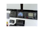 Boat helm panel with multiple navigation/display screens and a round gauge in the center, with throttle lever below.