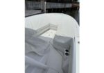 Open bow area of a white motorboat with cushioned seating and built-in storage, covered by a white canvas cover at a marina.