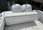 Back of a white boat showing two outboard engines and a folded rear storage seat on a clean deck near the water.