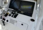 Boat helm cockpit with steering wheel, throttles, and two navigation screens showing a map and radar/sonar display (white console).