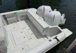 White boat deck with built‑in storage hatches and two large outboard engines at the stern, on calm water near a dock.