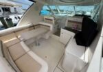 Luxurious yacht cockpit with beige L-shaped seating around a pedestal table; compact galley area with grill on the right.
