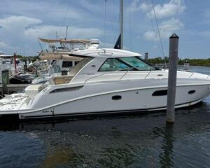 White motor yacht docked at a marina with other boats and calm water under a blue sky.
