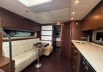 Interior of a luxury yacht: white leather sofa with a round table, galley with sink and dark wood cabinets, doorway to a sleeping cabin.