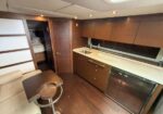 Boat galley with wood cabinetry, stainless sink, mini fridge, and a small round-table seating area; doorway to a sleeping cabin.