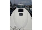 Bow view of a white yacht deck with an open hatch and cockpit behind, moored at a marina with other boats nearby.