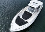 A white motorboat viewed from above on dark water, showing black cushioned bow seating and cockpit area.