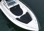 Top-down view of a white motorboat with black cushioned seating on the deck, floating in calm water.