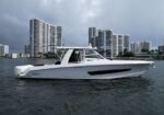 White luxury motor yacht on calm water with a skyline of tall modern buildings in the background.