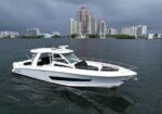 White motor yacht on calm water with a city skyline of high-rise buildings behind.