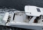 Top-down view of a white motorboat with twin outboard engines at the stern, open cockpit, and a solar panel on the cabin roof on dark water.