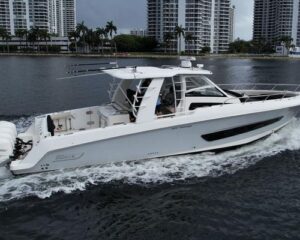 2020-boston-whaler-420-outrage-power-10189752-20260520065249929-2 | Boat Universe White luxury motor yacht cruising on calm water with a city skyline of high-rise buildings in the background; passengers visible on the deck under a shaded cabin.