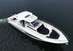 Aerial view of a white motorboat cruising on dark blue water, showing an open cockpit and sun deck from above.