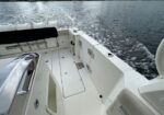Rear deck of a white motorboat with storage hatches and stainless rails, open water and wake in the background