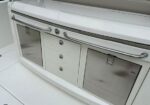 White marine galley cabinet with two stainless steel doors on either side and a central row of three drawers, set into a white deck.