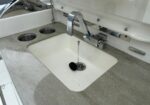 Boat galley sink with chrome faucet and white square basin set in a gray speckled countertop; two circular cup holders to the left and a drain plug on a chain in the sink.