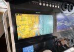 Boat cockpit with two navigation screens: left shows an electronic nautical chart (yellow land, blue water), right shows sonar imagery/graphing.