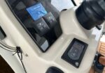 Close-up of a boat helm showing a control panel with a digital display, toggle switches, and a blue ID card mounted nearby.