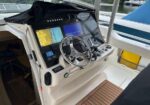 Boat helm with steering wheel, navigation screens, and throttle levers at a dockside cockpit.