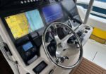 Boat cockpit with a chrome steering wheel and three navigation screens showing a map and radar data at the helm at sea.
