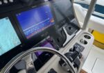 Boat helm with multiple navigation screens displaying charts and sonar, stainless steering wheel in foreground, cup holders and controls nearby.