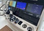 Boat cockpit helm with three large display screens, steering wheel, throttle levers, and cup holders.