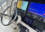Boat helm with stainless steering wheel and multiple navigation screens displaying map and sonar data on a boat cockpit panel.
