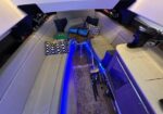 L-shaped beige sofa with blue patterned pillows around a small wooden table; blue LED lighting highlights a compact yacht bar and kitchenette.