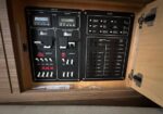 Open wooden cabinet housing an RV electrical panel with switches, breakers, and two digital meters labeled shore power.