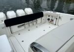 White boat cockpit with a black rear bench, rod holders and storage; three outboard motors at the stern and calm water in the background.