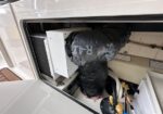Boat air conditioner unit installed in a cabin/compartment with insulated ducting and exposed hoses nearby.