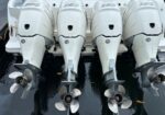 Four white outboard boat engines with stainless propellers mounted on a stern, labeled 350, in a marina setting.